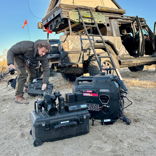 Person setting Flex Power portable generator in front of a overland truck with a roof top tent on a clear day